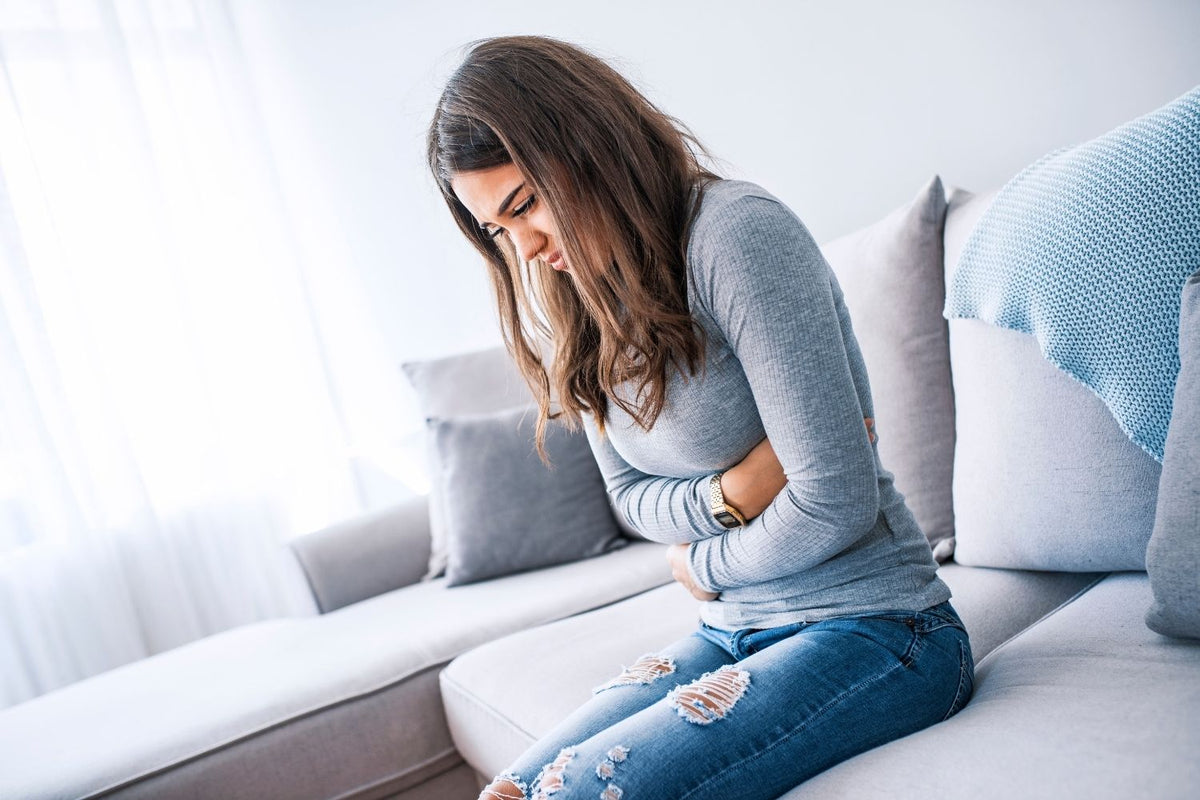 Frau hält sich den Bauch vor Schmerzen – Symbolbild für Nahrungsmittelunverträglichkeiten bei Hashimoto“