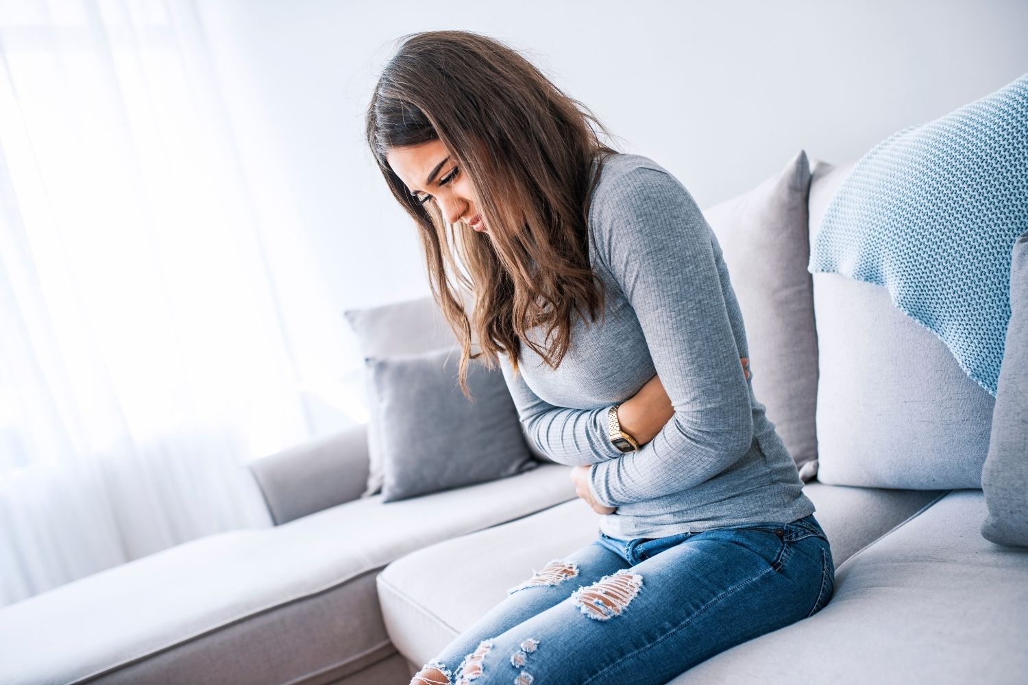 Frau hält sich den Bauch vor Schmerzen – Symbolbild für Nahrungsmittelunverträglichkeiten bei Hashimoto“
