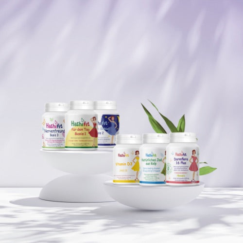 Hashifit Unterstützungspaket mit Basis 1, Basis 2, Basis 3, Vitamin D3, Jod aus Kelp und Darmflora 16 Plus auf weißen Podesten vor zartlila Hintergrund